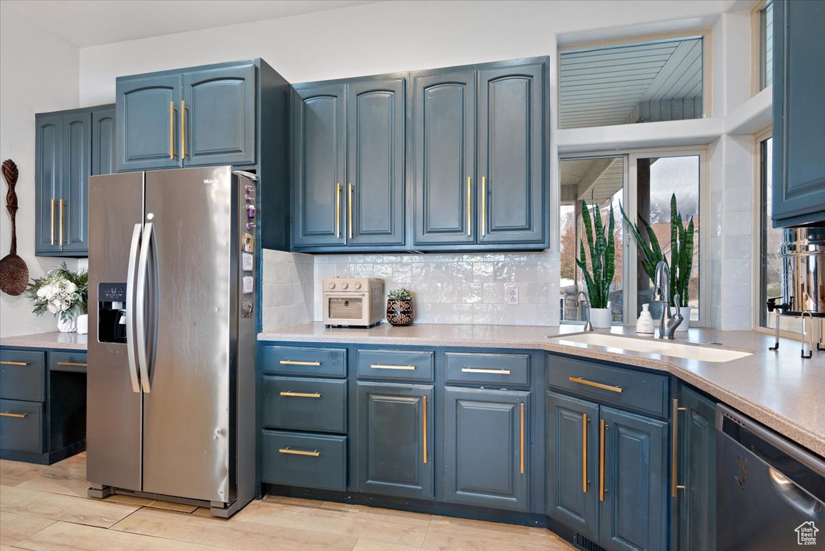 Kitchen with light wood-type flooring, blue cabinets, sink, and appliances with stainless steel finishes