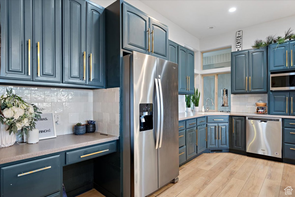 Kitchen with blue cabinets, light wood-type flooring, sink, and appliances with stainless steel finishes