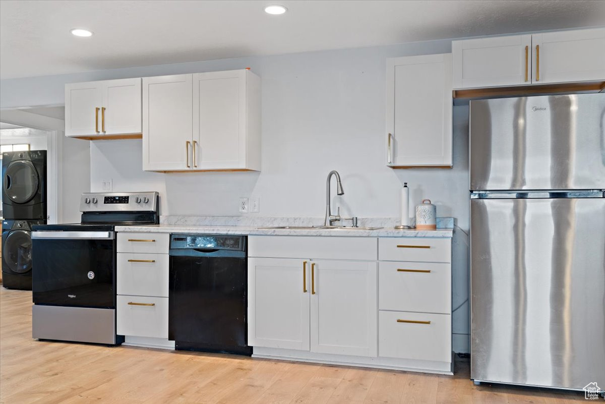 Kitchen featuring white cabinetry, sink, stacked washing maching and dryer, stainless steel appliances, and light hardwood / wood-style floors