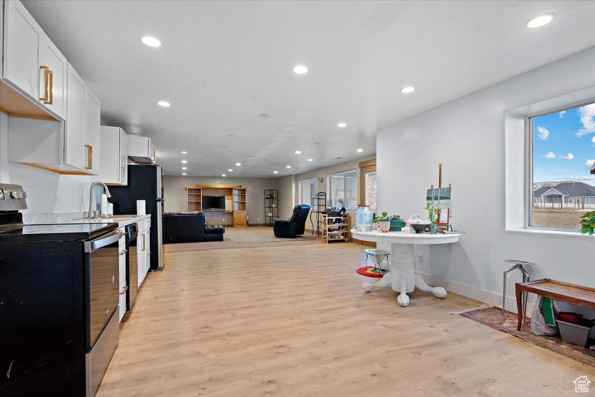 Kitchen featuring white cabinetry, sink, black dishwasher, electric stove, and light wood-type flooring