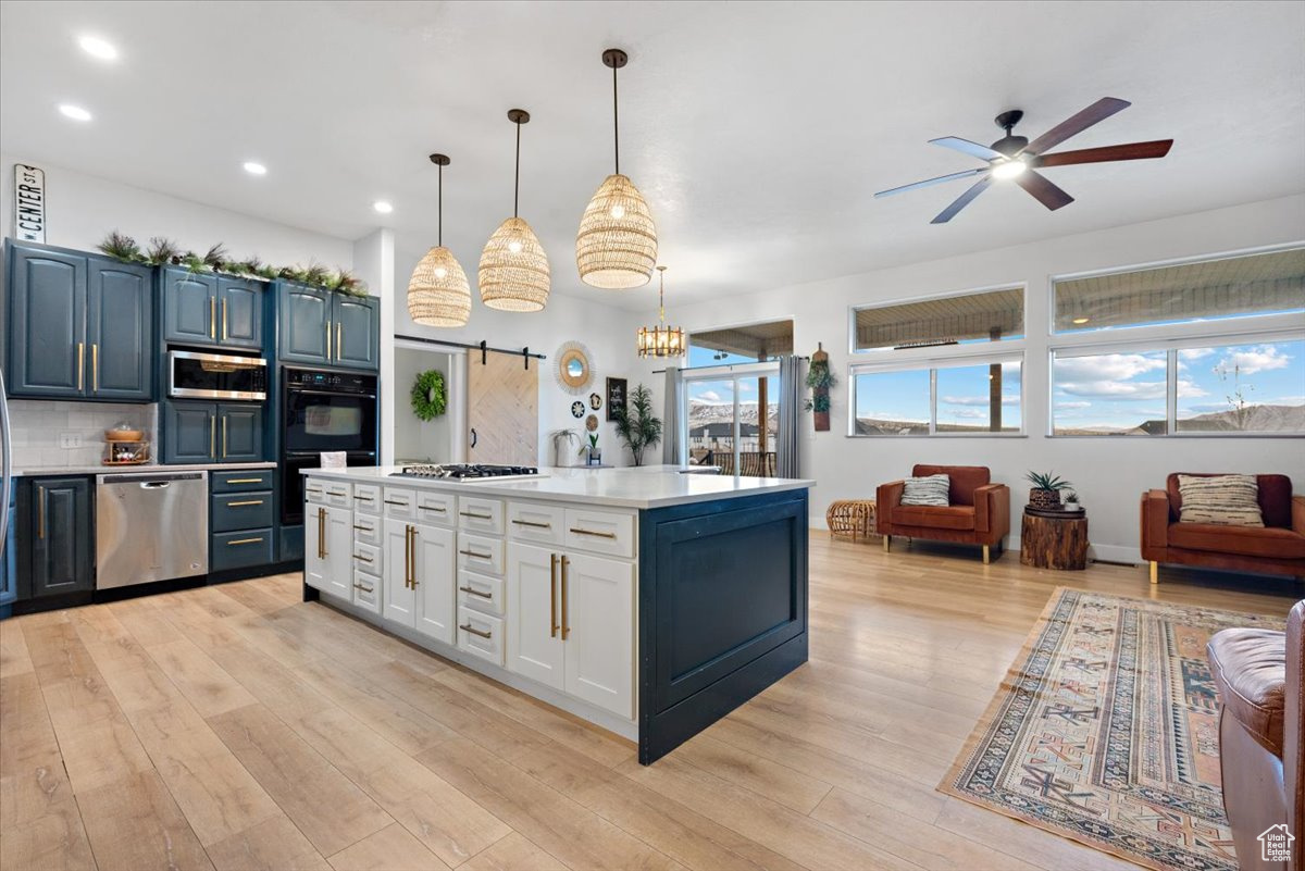 Kitchen featuring hanging light fixtures, a barn door, light wood-type flooring, blue cabinetry, and stainless steel appliances