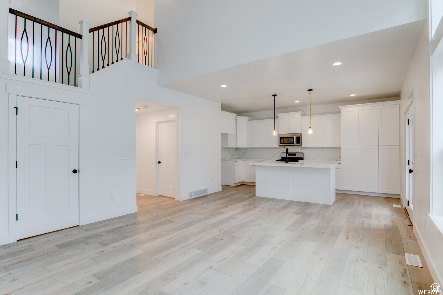 Kitchen featuring white cabinetry, an island with sink, stainless steel appliances, and decorative light fixtures