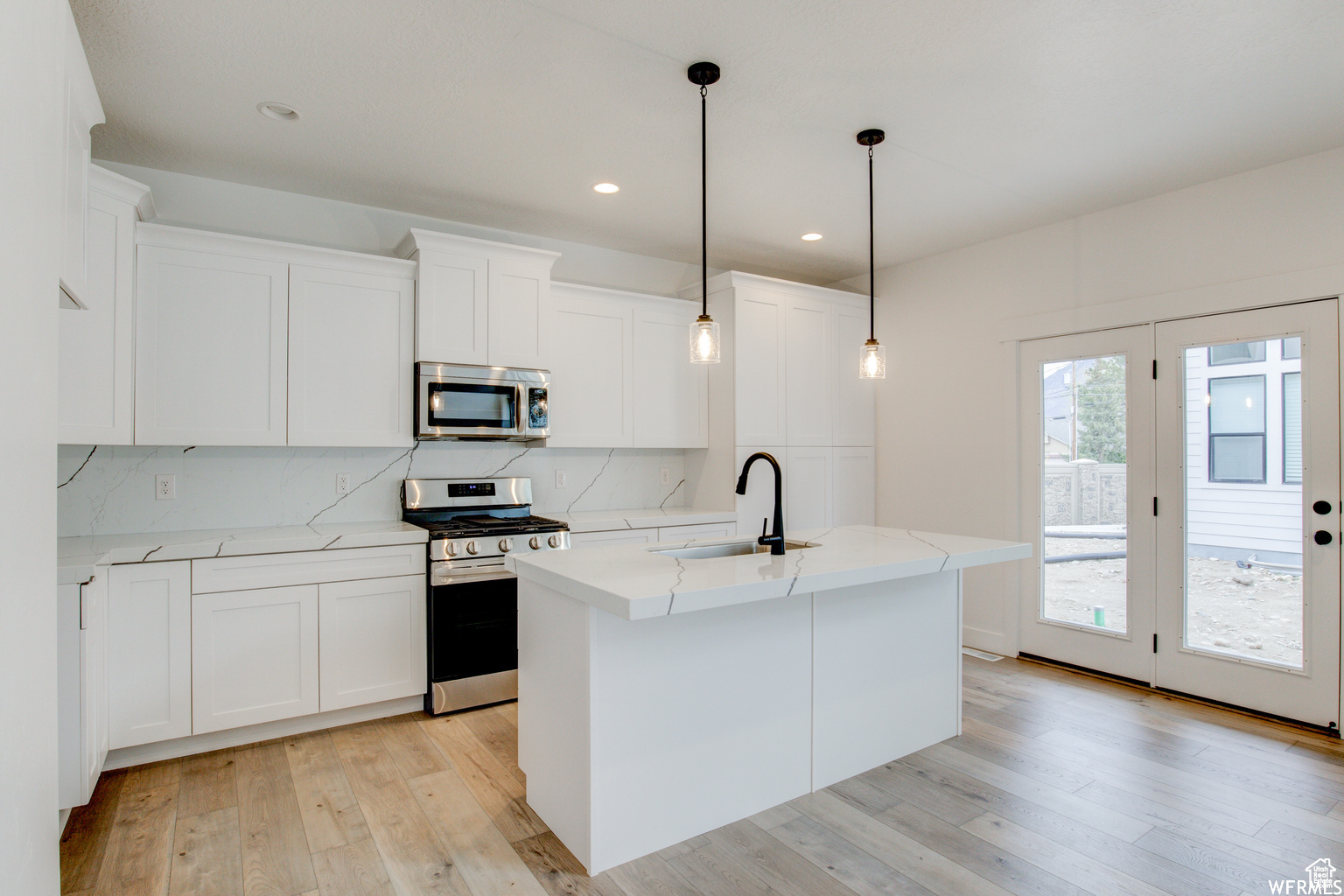 Kitchen with white cabinets, a kitchen island with sink, sink, and appliances with stainless steel finishes