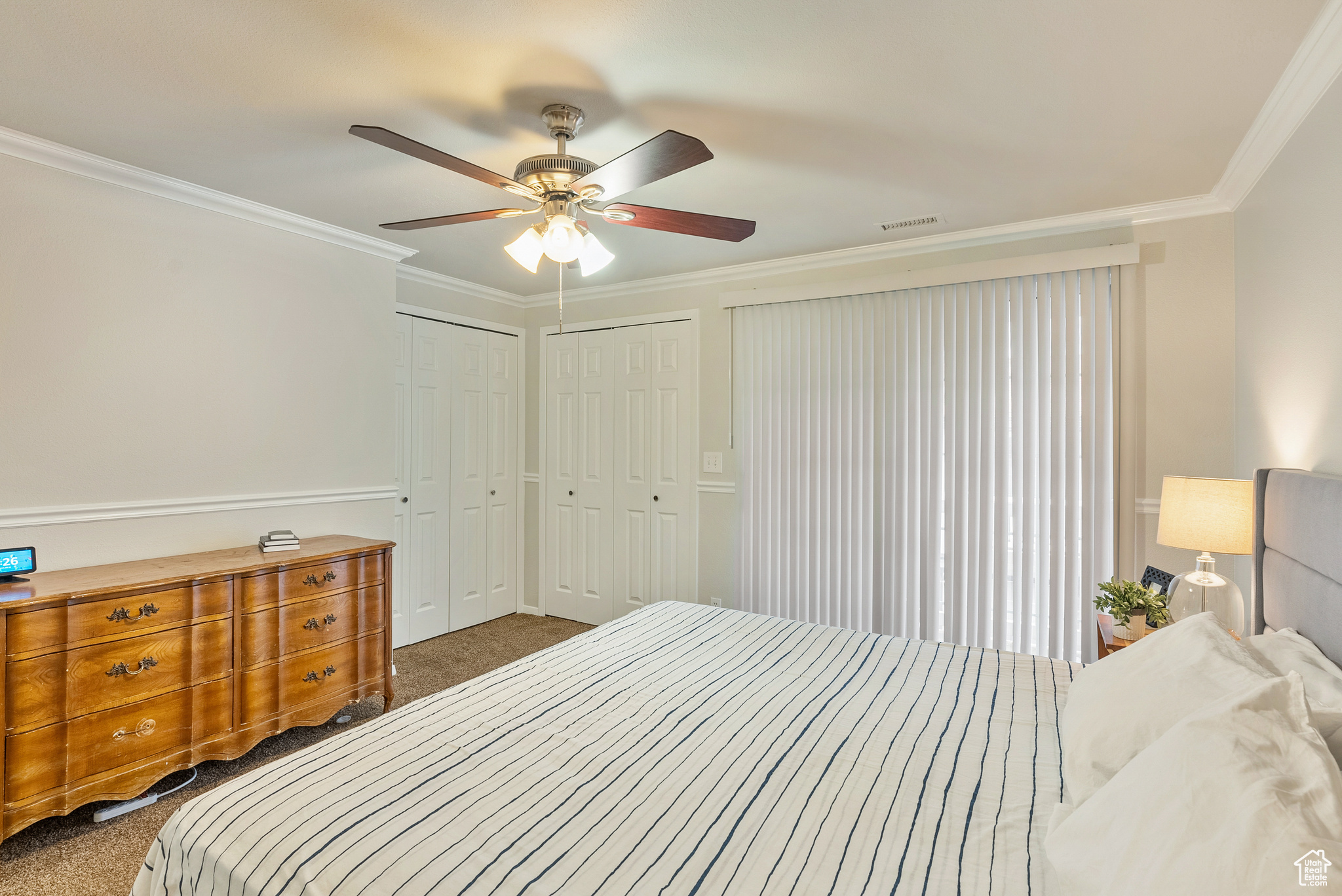 Carpeted bedroom featuring multiple closets, ceiling fan, and ornamental molding