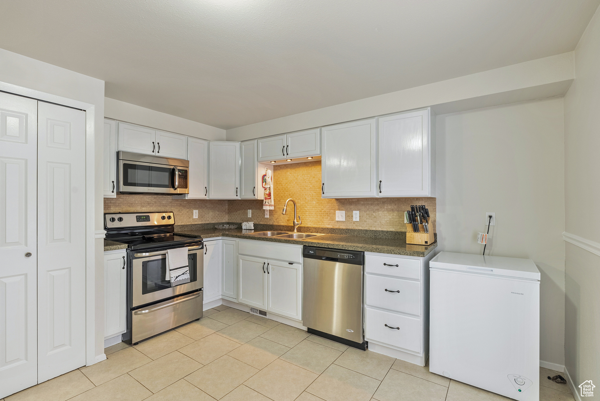 Kitchen with white cabinets, appliances with stainless steel finishes, tasteful backsplash, and sink