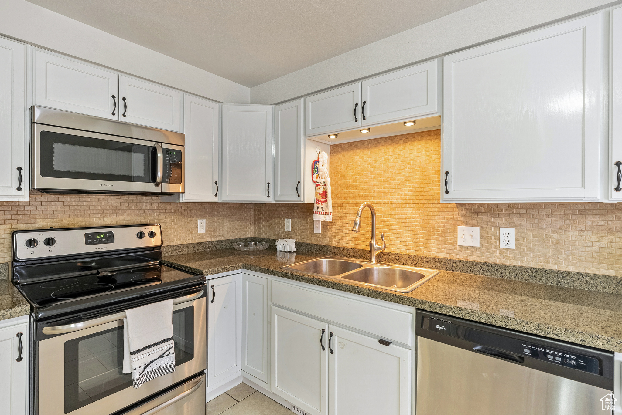 Kitchen featuring white cabinets, sink, decorative backsplash, appliances with stainless steel finishes, and light tile patterned flooring