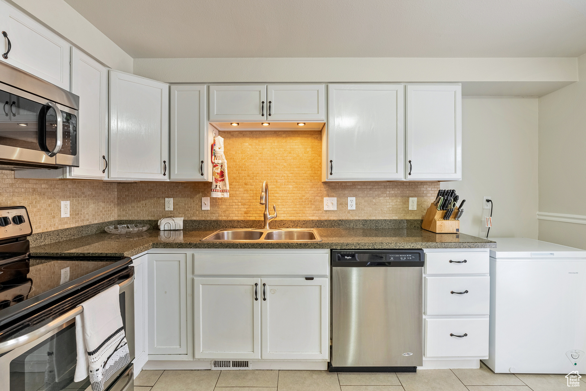 Kitchen featuring appliances with stainless steel finishes, backsplash, white cabinetry, and sink