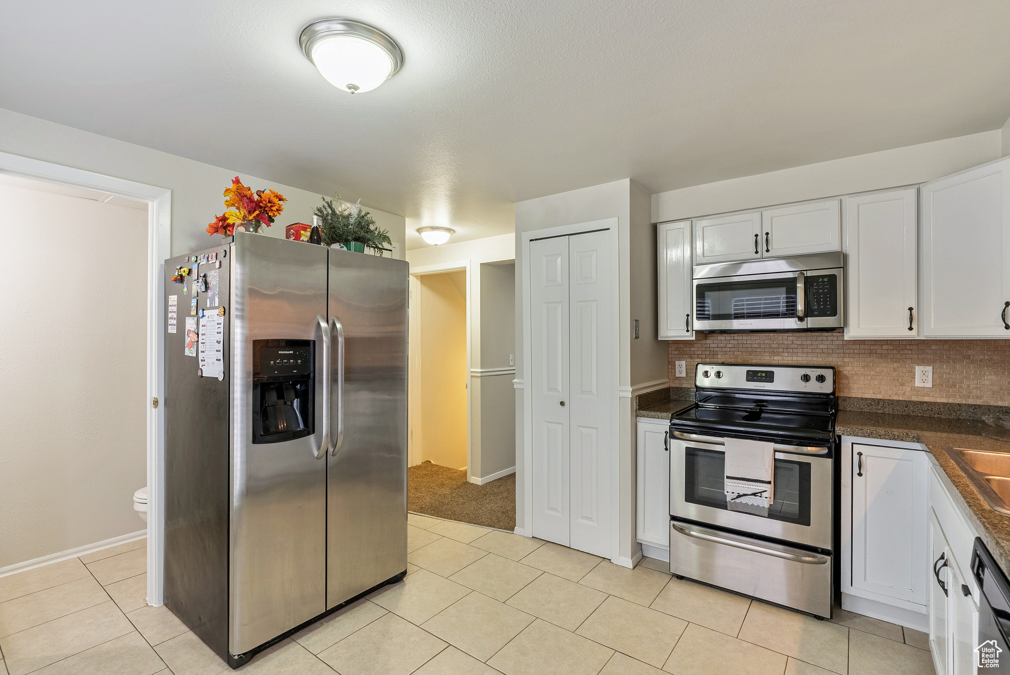 Kitchen with backsplash, white cabinetry, light tile patterned flooring, and stainless steel appliances