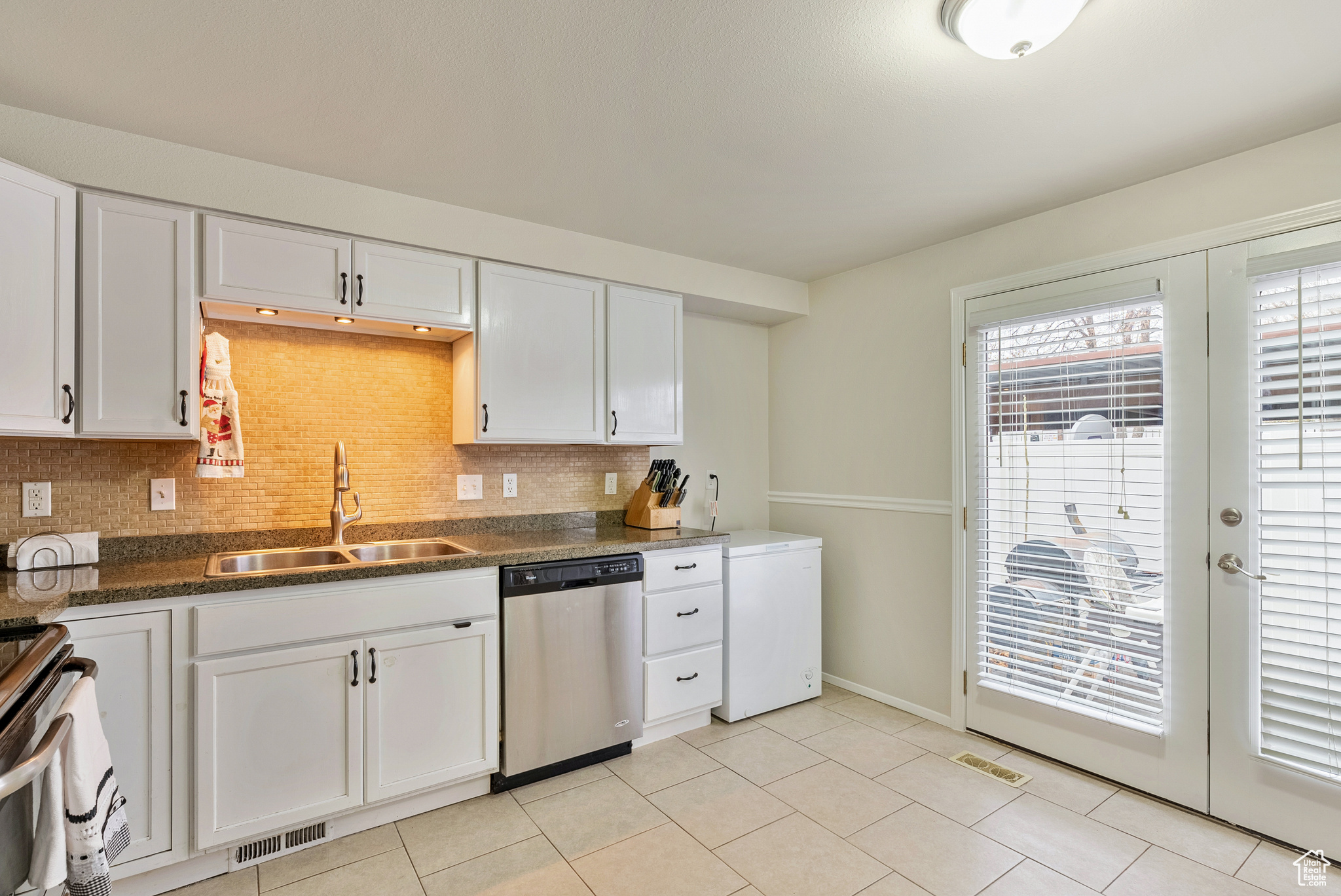 Kitchen featuring stainless steel dishwasher, backsplash, white cabinetry, and sink