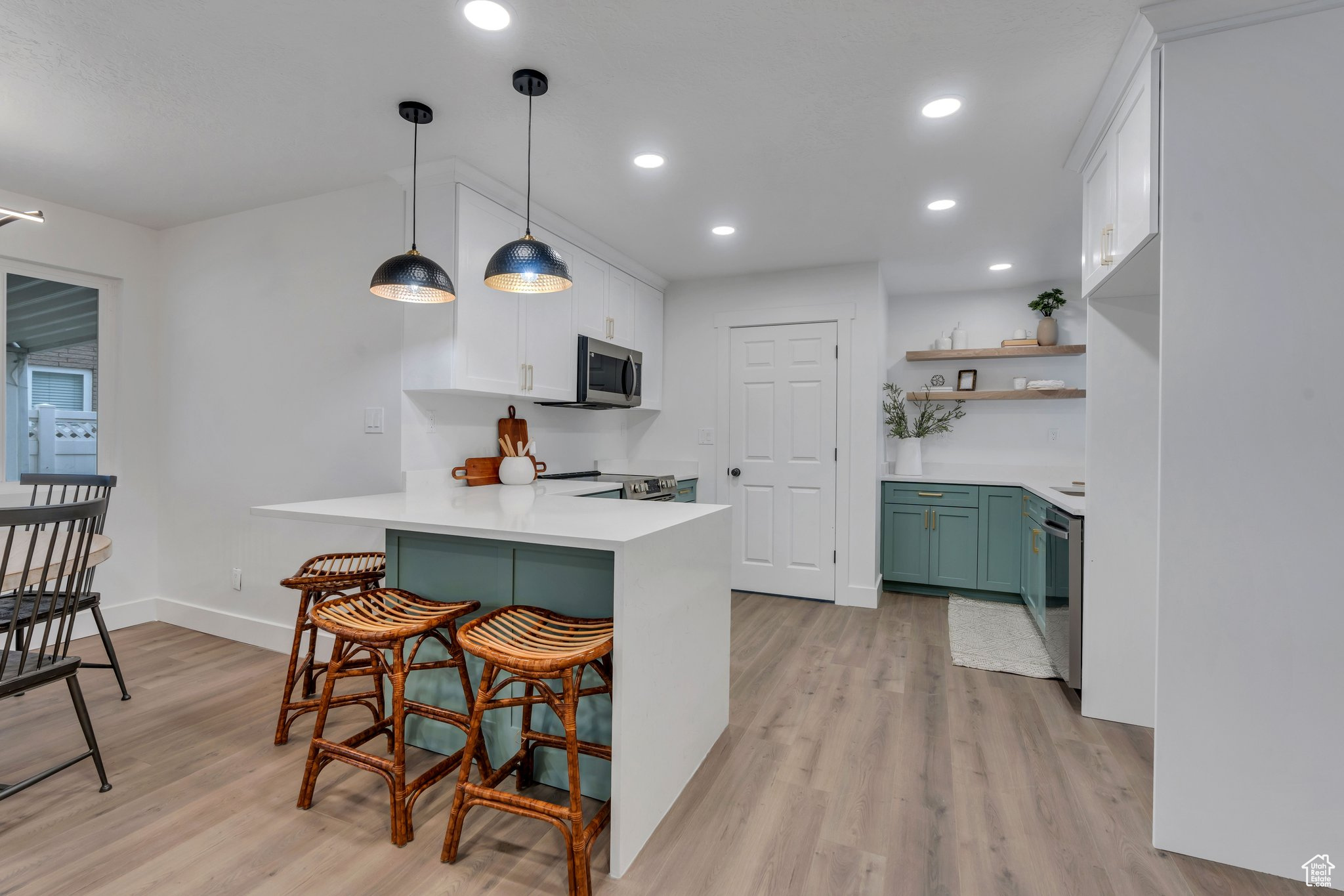 Kitchen with kitchen peninsula, light wood-type flooring, pendant lighting, white cabinets, and a breakfast bar area