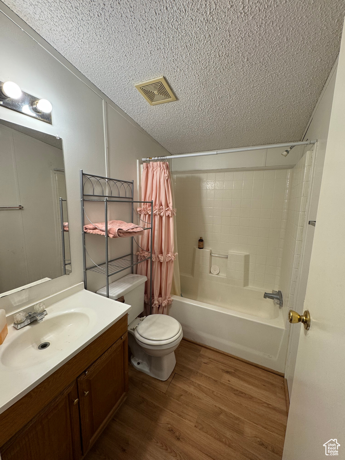 Full bathroom with shower / bathtub combination with curtain, hardwood / wood-style floors, a textured ceiling, toilet, and vanity