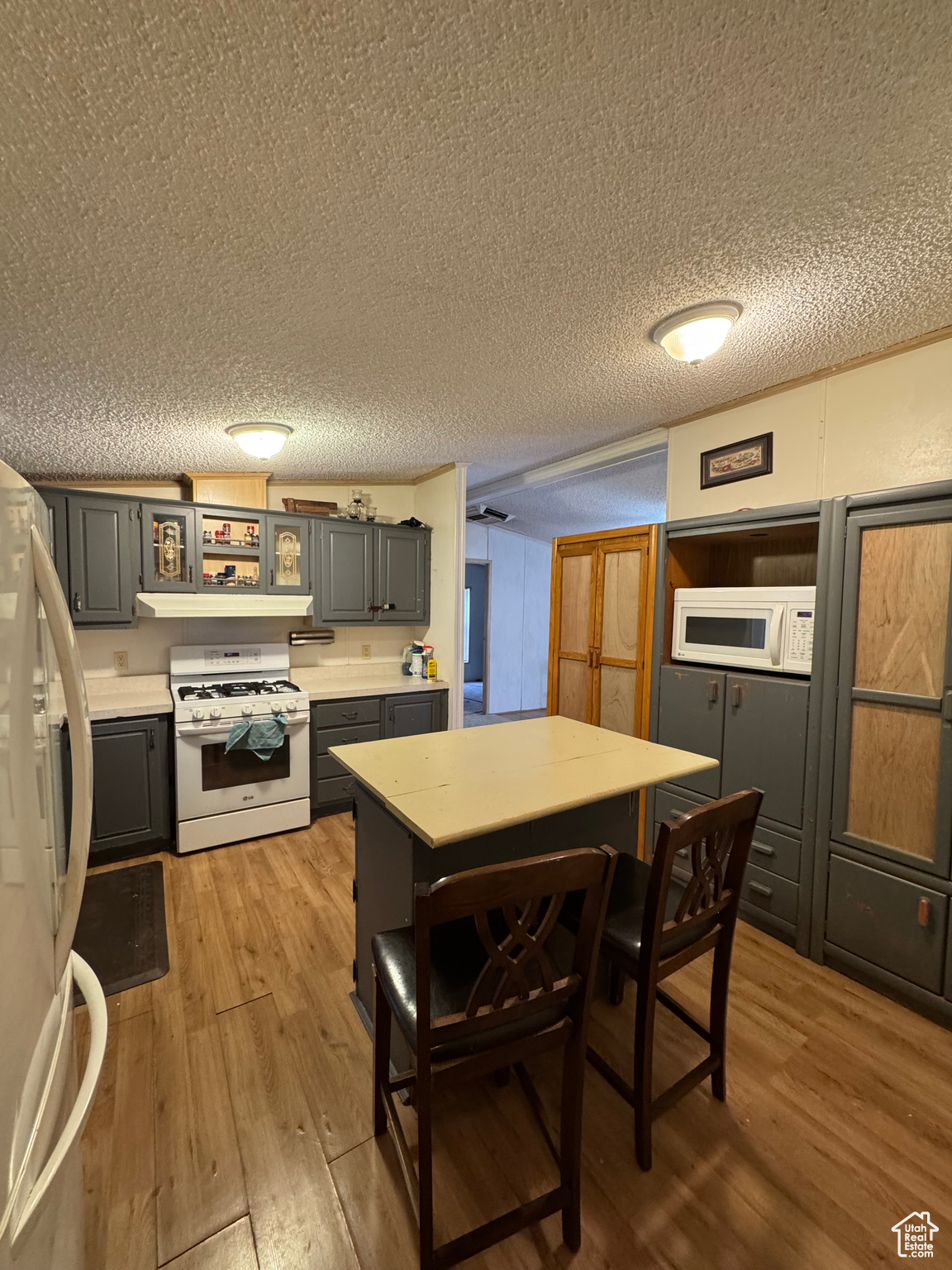 Kitchen with gray cabinetry, light wood-type flooring, white appliances, and a textured ceiling