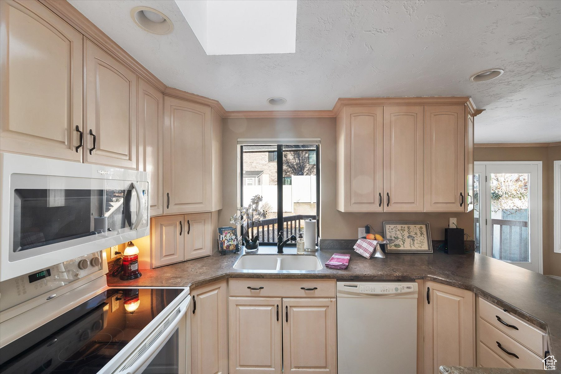 Kitchen with blonde cabinetry, smooth top range & solid surface counters