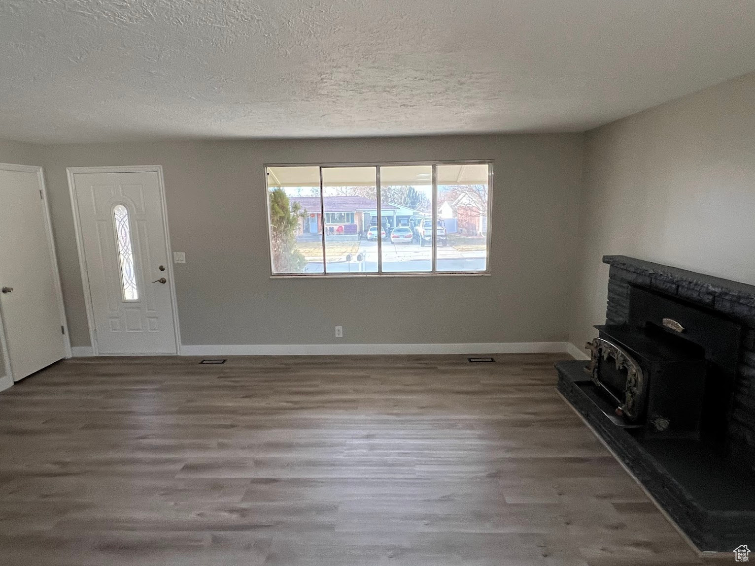 Unfurnished living room with a textured ceiling, light hardwood / wood-style floors, and a wood stove