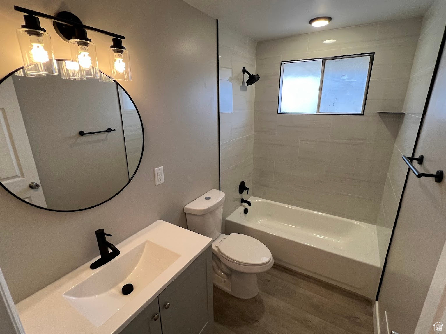 Full bathroom with tiled shower / bath combo, toilet, wood-type flooring, and vanity