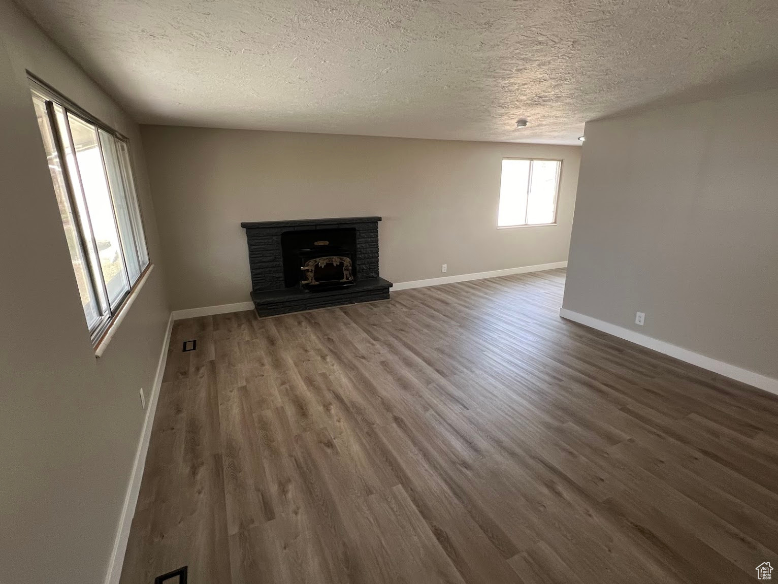 Unfurnished living room with hardwood / wood-style floors, a textured ceiling, and a brick fireplace