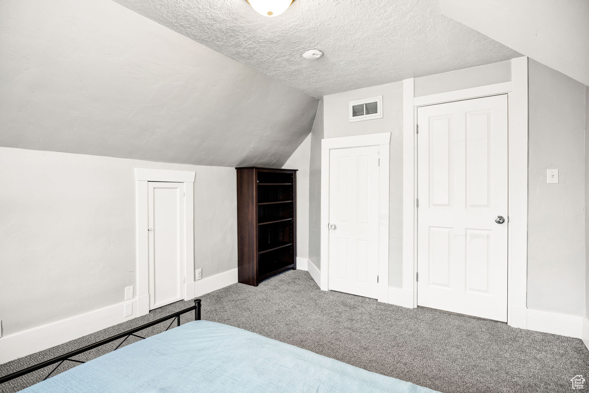 Carpeted bedroom with a textured ceiling and vaulted ceiling