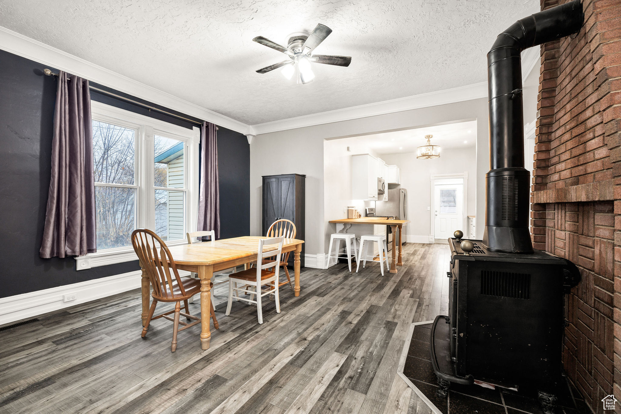 Dining area with a wood stove, crown molding, ceiling fan with notable chandelier, and hardwood / wood-style flooring