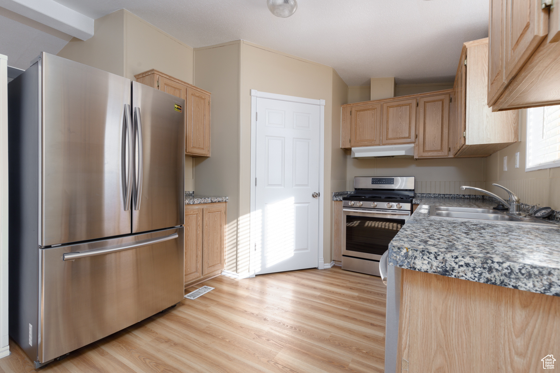 Kitchen with sink, stainless steel appliances, light brown cabinets, and light hardwood / wood-style floors