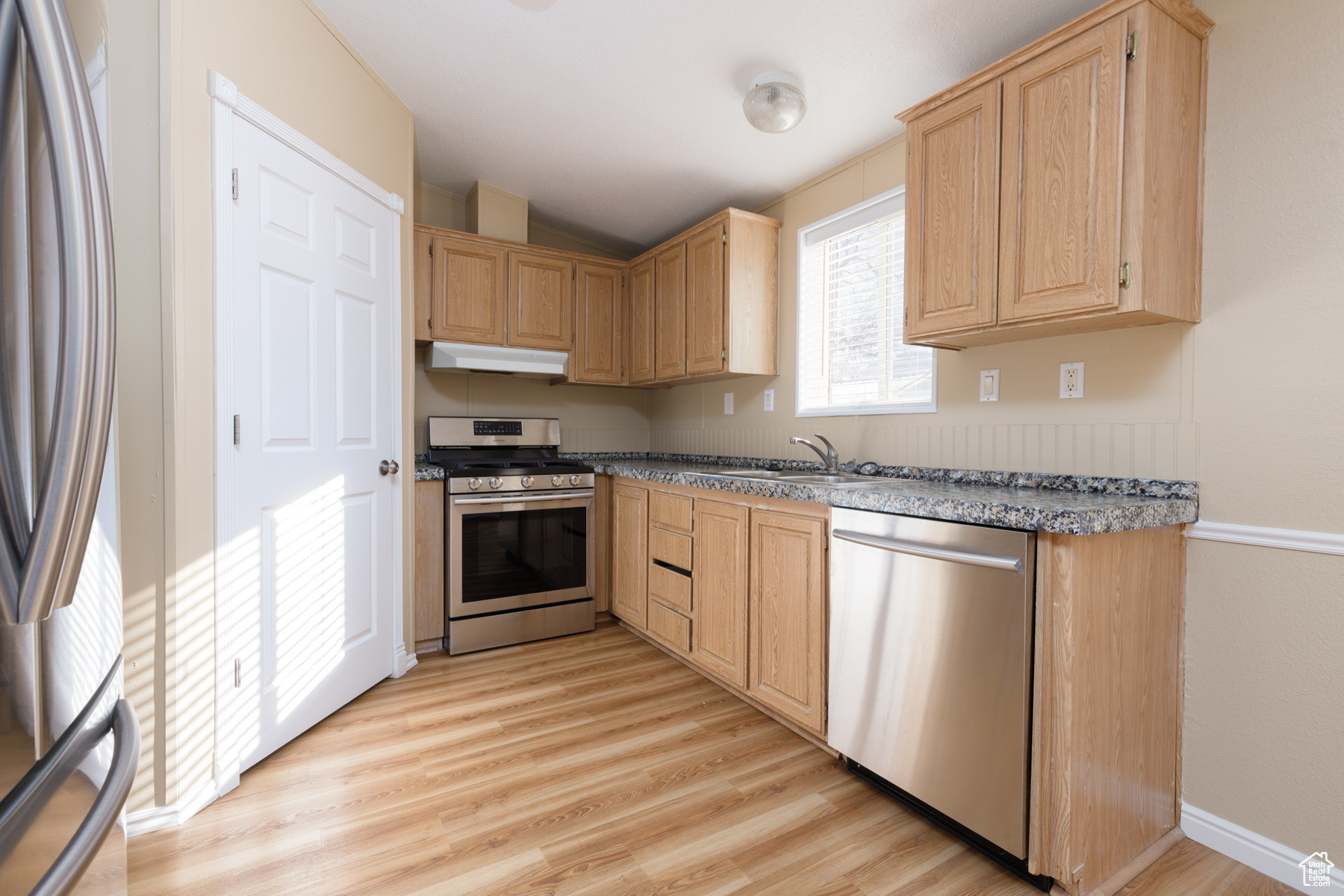 Kitchen featuring light wood-type flooring, light brown cabinetry, sink, and appliances with stainless steel finishes