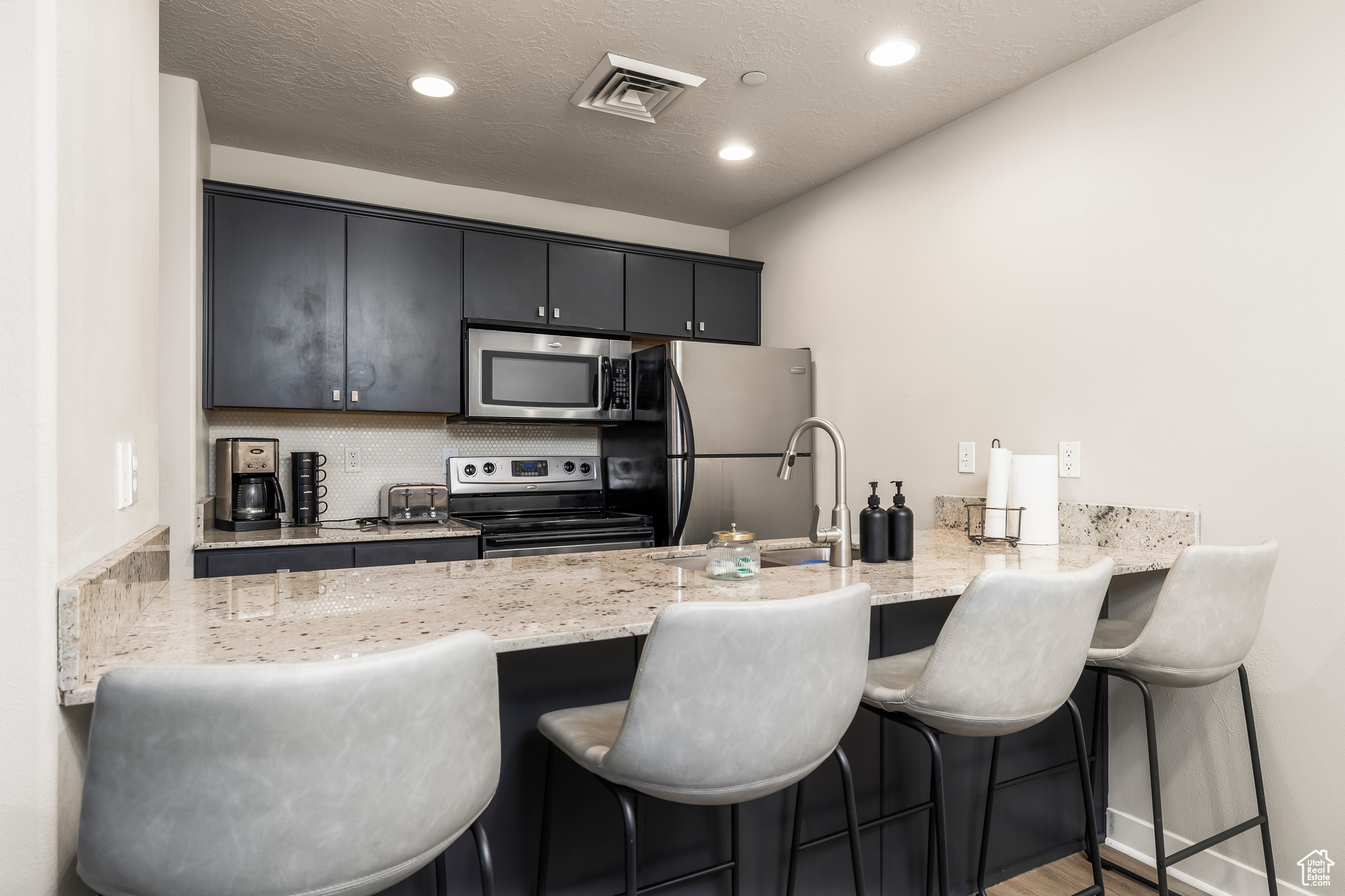 Kitchen with a breakfast bar, light stone counters, kitchen peninsula, and stainless steel appliances