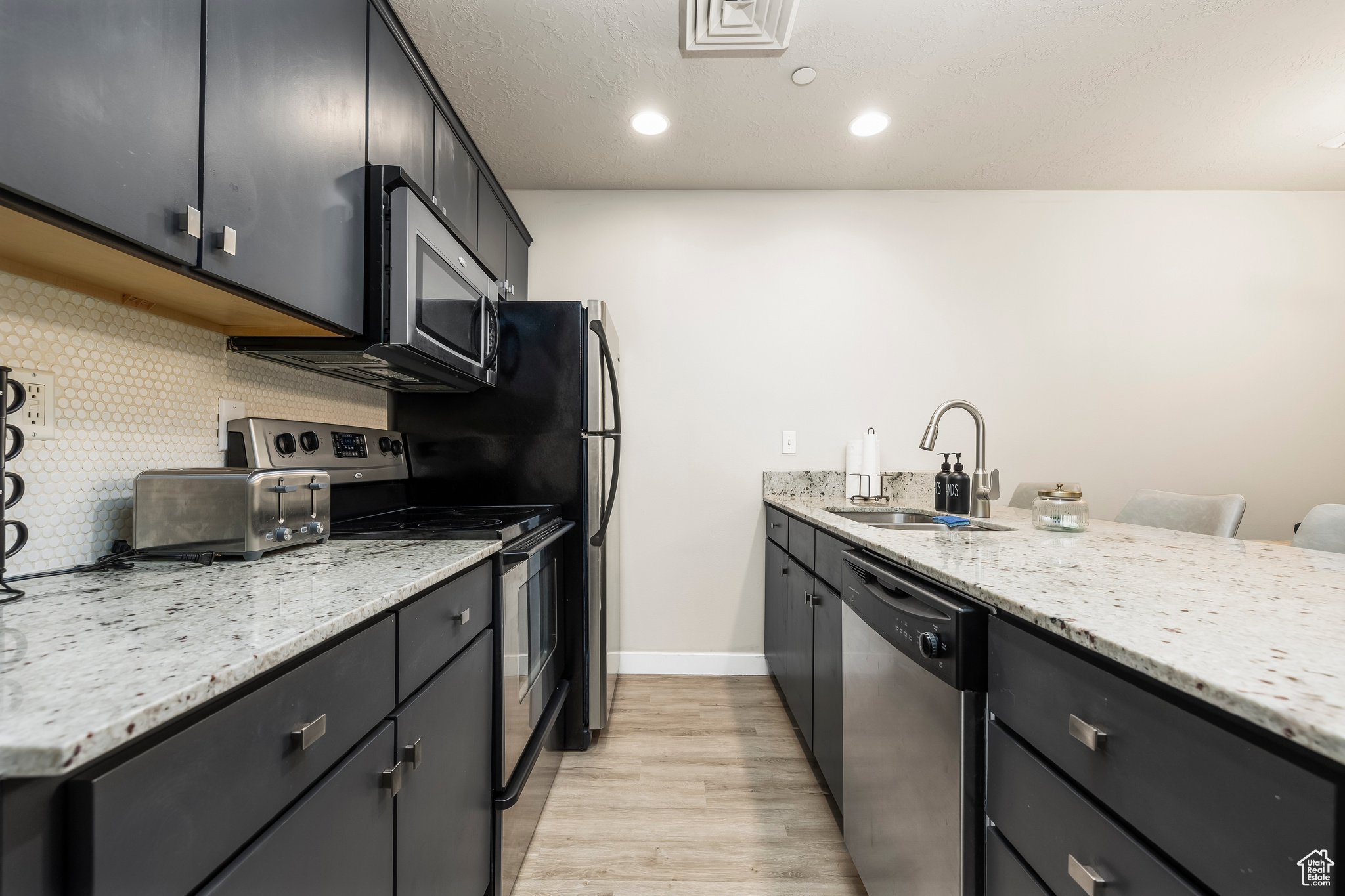 Kitchen featuring backsplash, sink, light hardwood / wood-style flooring, appliances with stainless steel finishes, and light stone counters