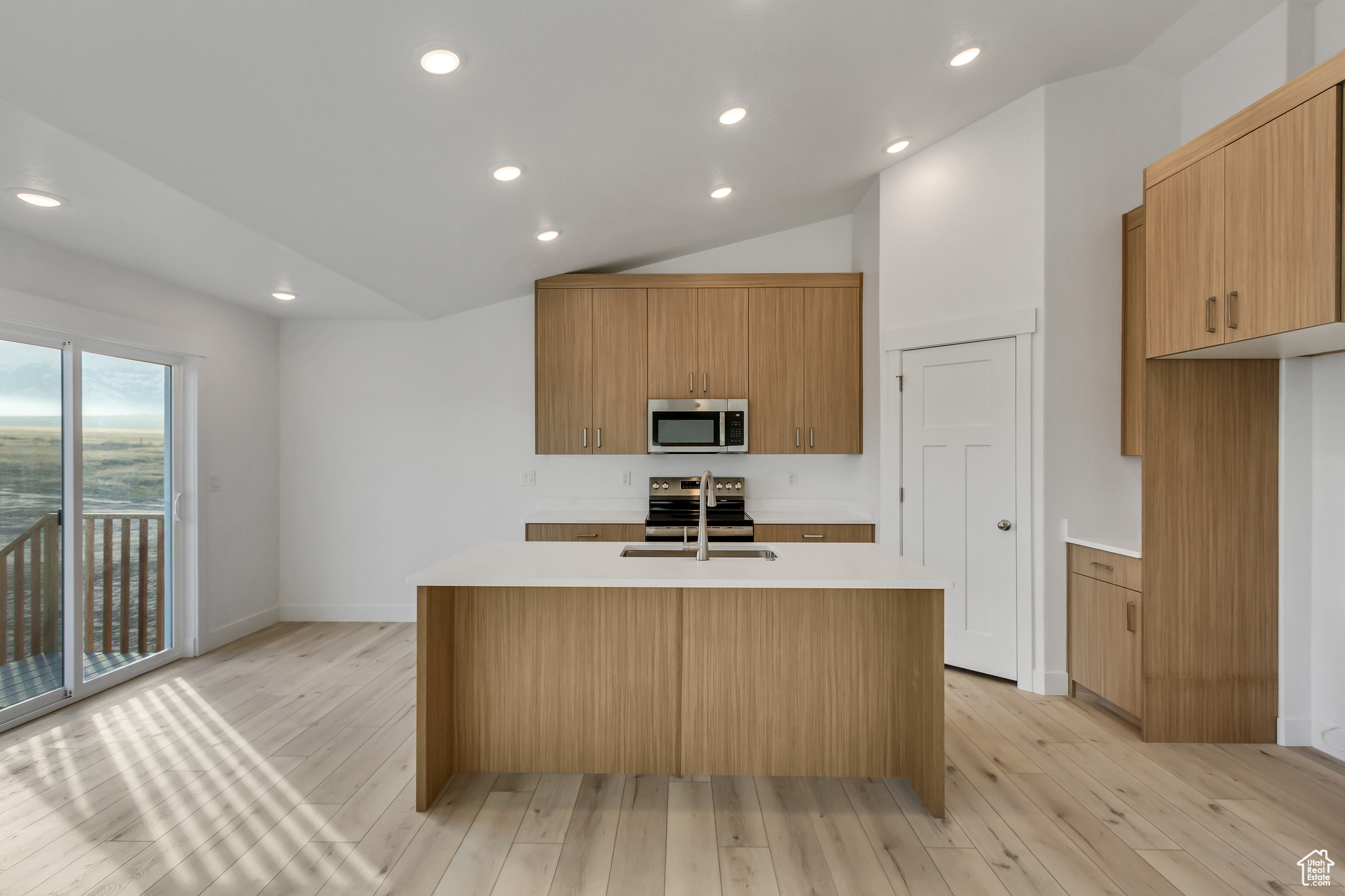 Kitchen with appliances with stainless steel finishes, light wood-type flooring, a center island with sink, and lofted ceiling