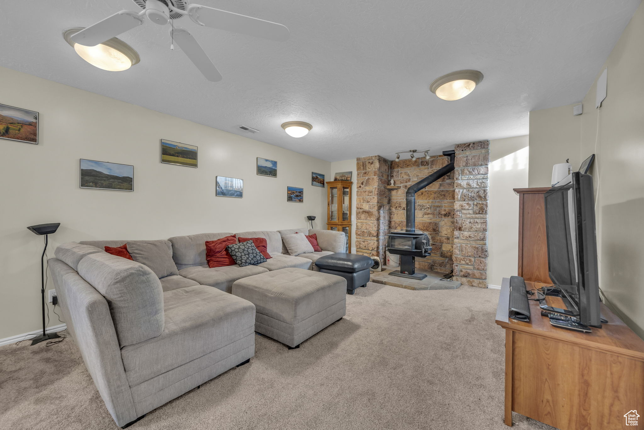 Living room featuring a wood stove, ceiling fan, and light colored carpet