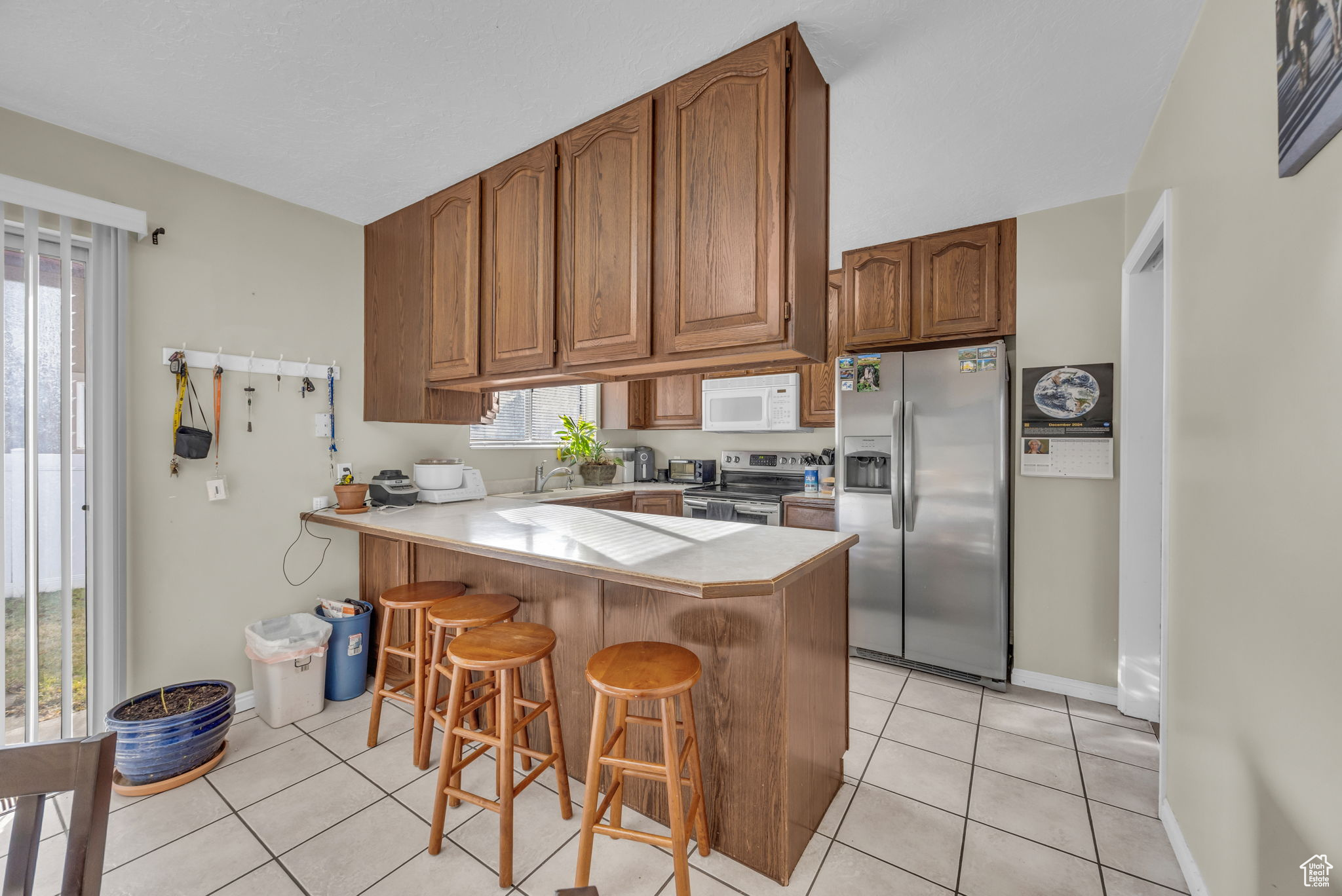 Kitchen with sink, kitchen peninsula, a breakfast bar, light tile patterned flooring, and appliances with stainless steel finishes