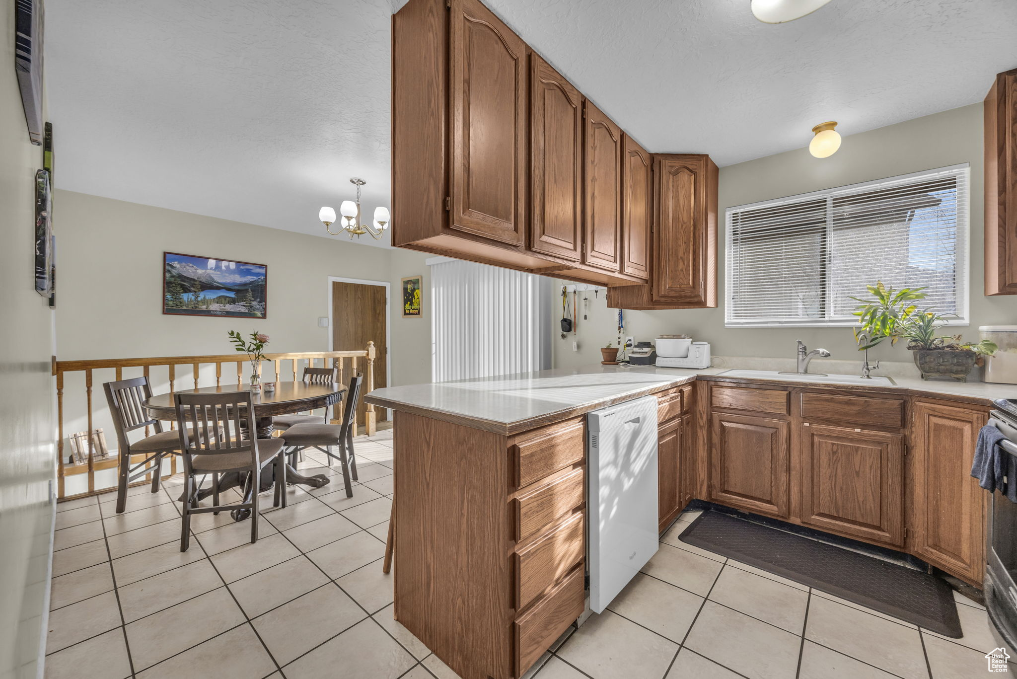 Kitchen with kitchen peninsula, white dishwasher, sink, a notable chandelier, and light tile patterned flooring