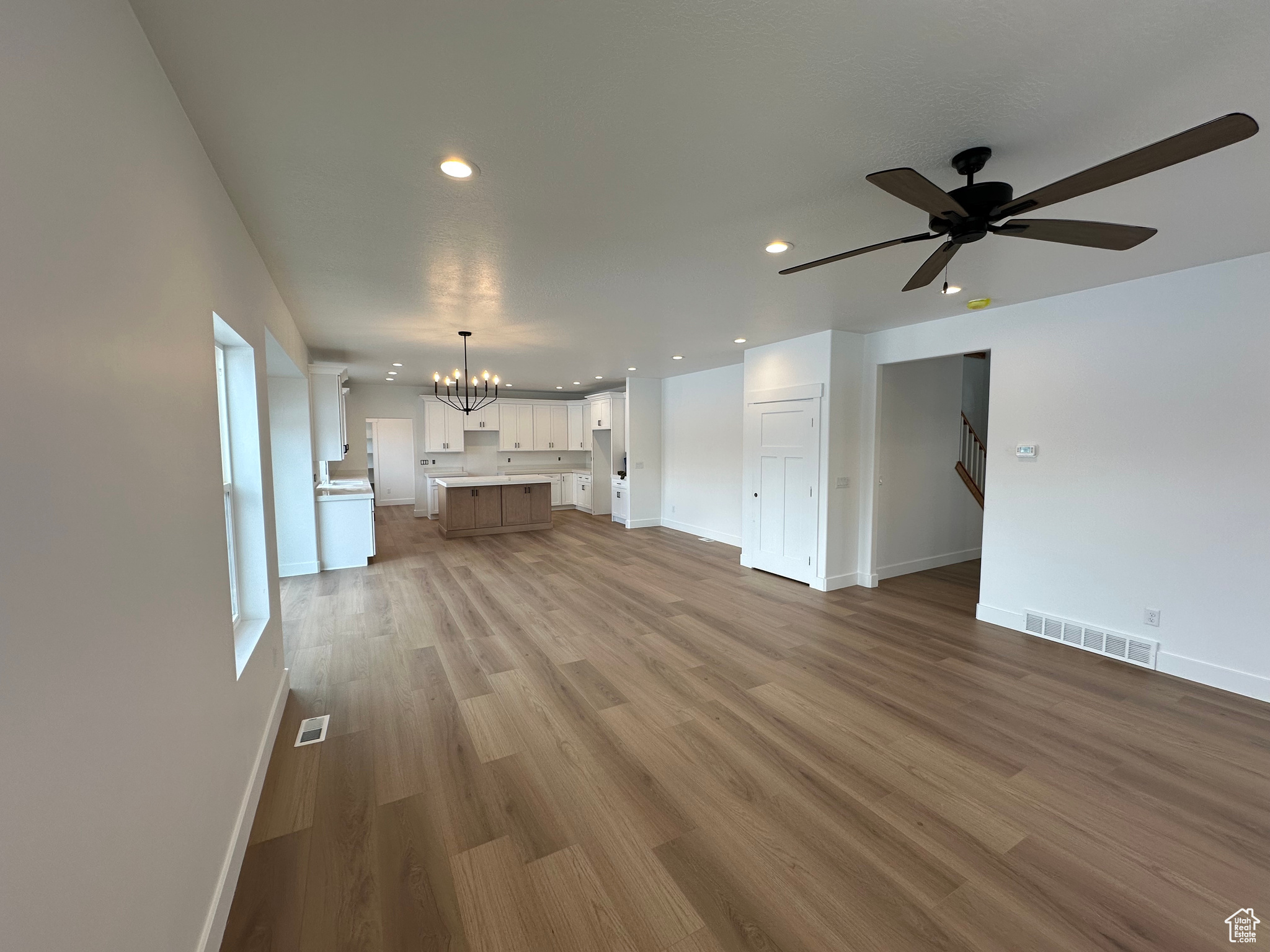 Kitchen with laminate flooring, chandelier over dining area, white cabinets, a center island, quartz countertops, crown moulding.