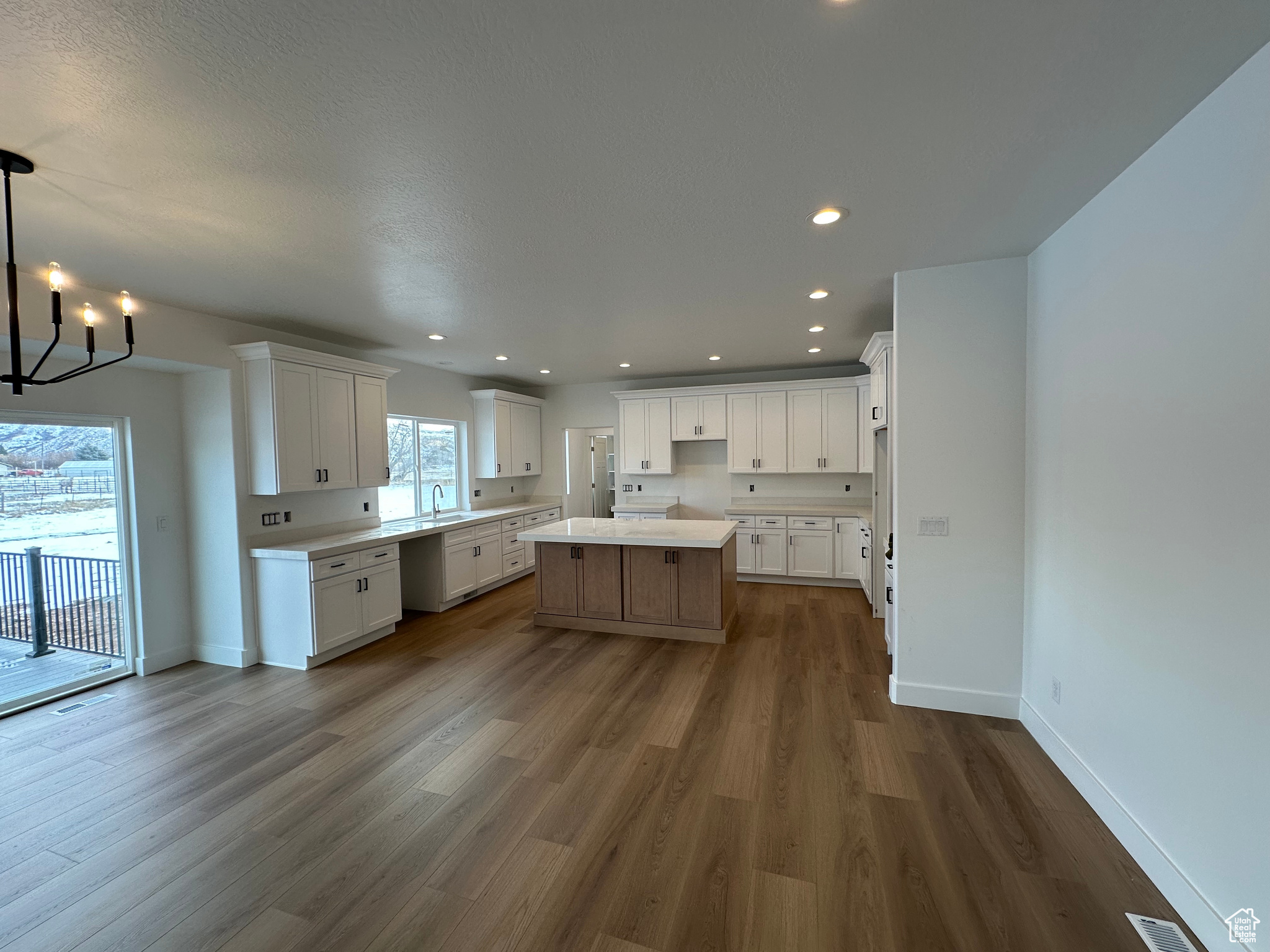 Kitchen with laminate flooring, chandelier over dining area, white cabinets, a center island, quartz countertops, crown moulding.