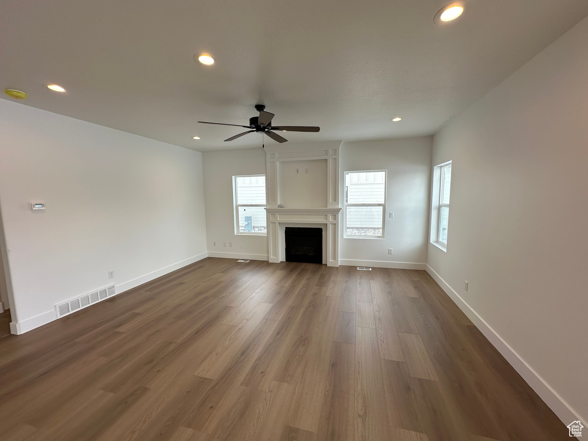 Family room featuring laminate flooring and ceiling fan. Gas fireplace with mantle and window set.