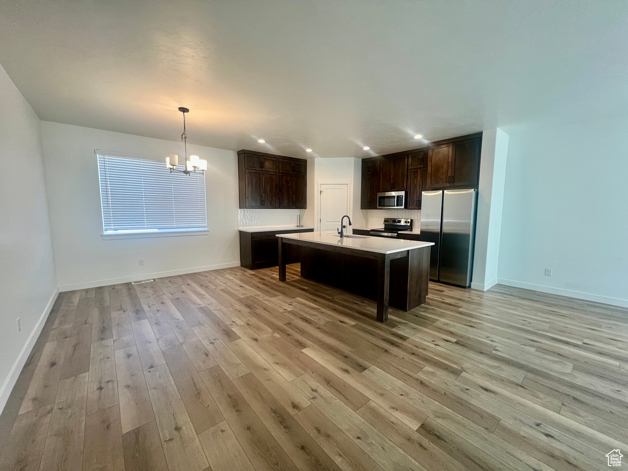 Kitchen with pendant lighting, sink, light hardwood / wood-style flooring, an island with sink, and appliances with stainless steel finishes