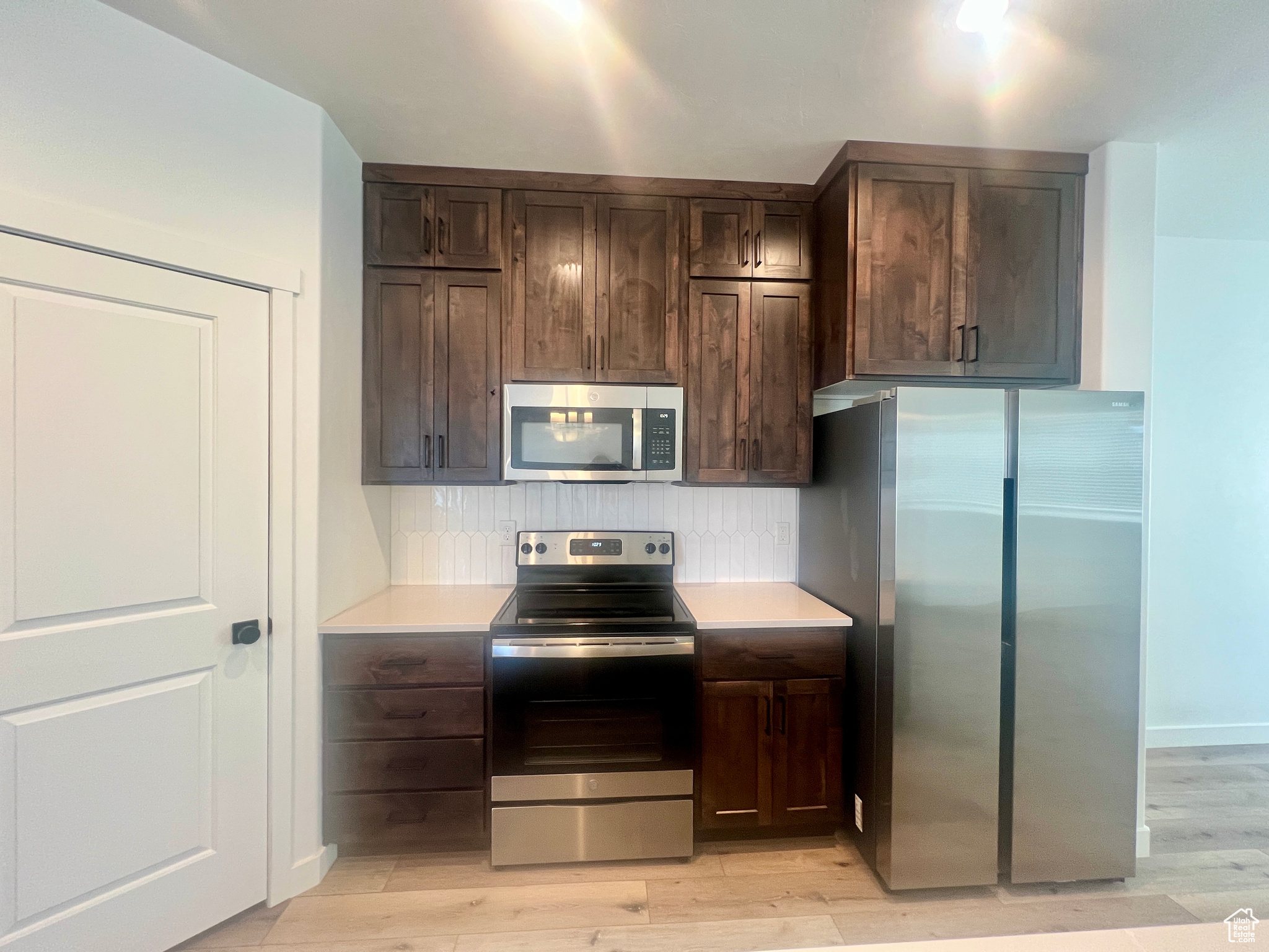 Kitchen with appliances with stainless steel finishes, dark brown cabinetry, tasteful backsplash, and light hardwood / wood-style flooring