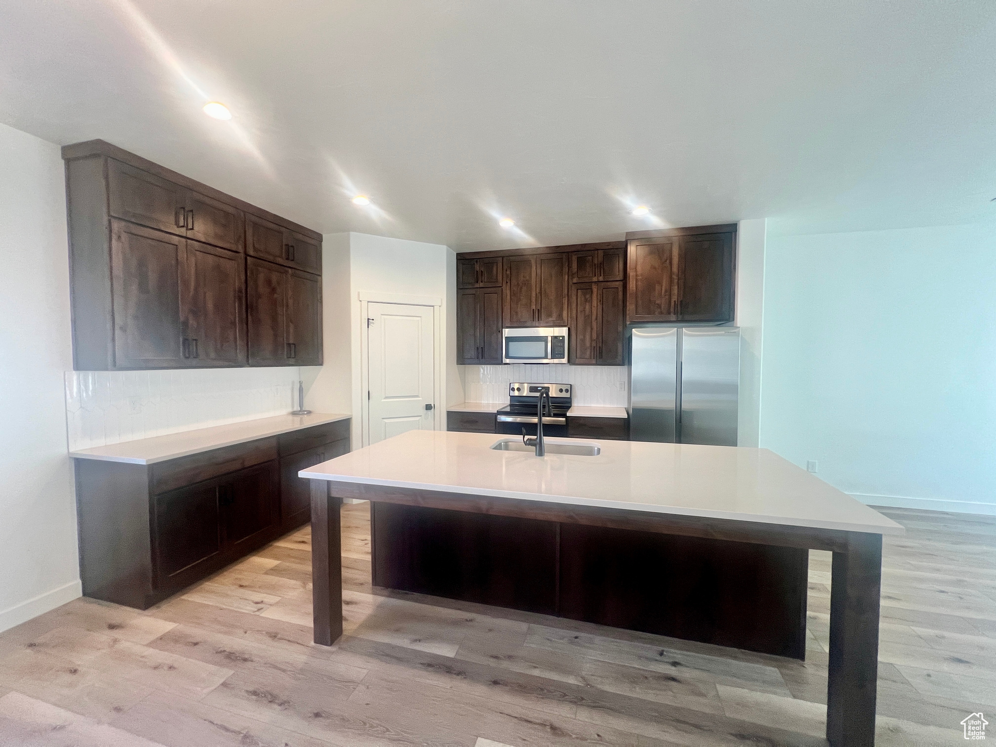 Kitchen featuring dark brown cabinets, stainless steel appliances, a kitchen island with sink, and sink