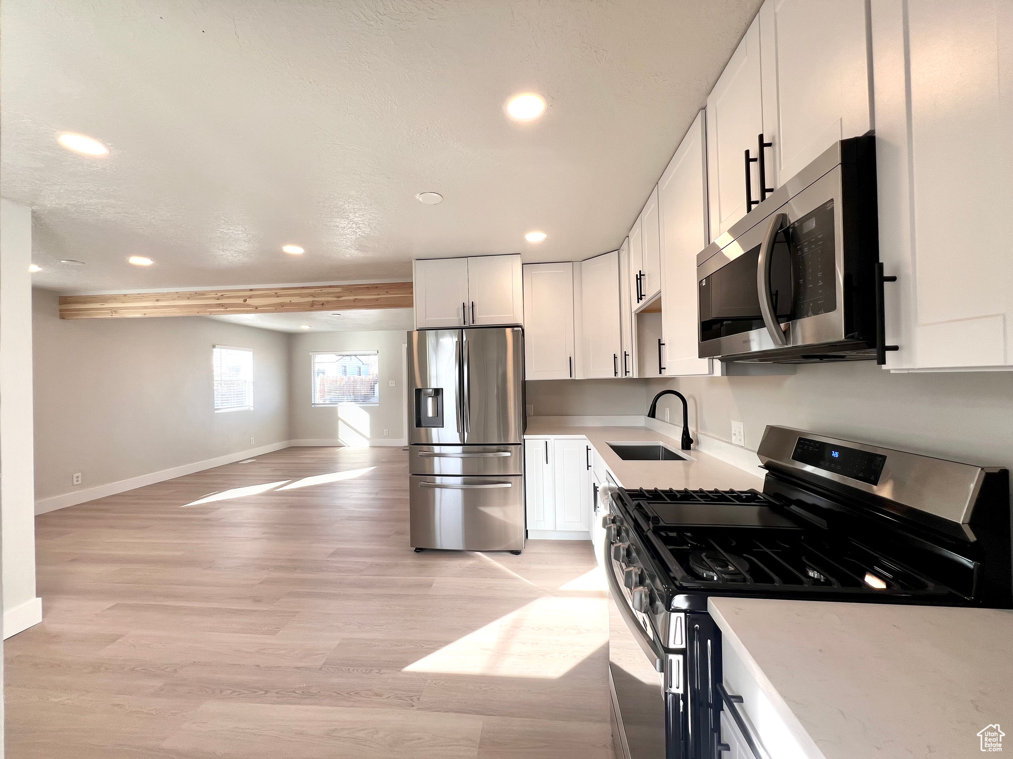 Kitchen with appliances with stainless steel finishes, light wood-type flooring, sink, beamed ceiling, and white cabinets