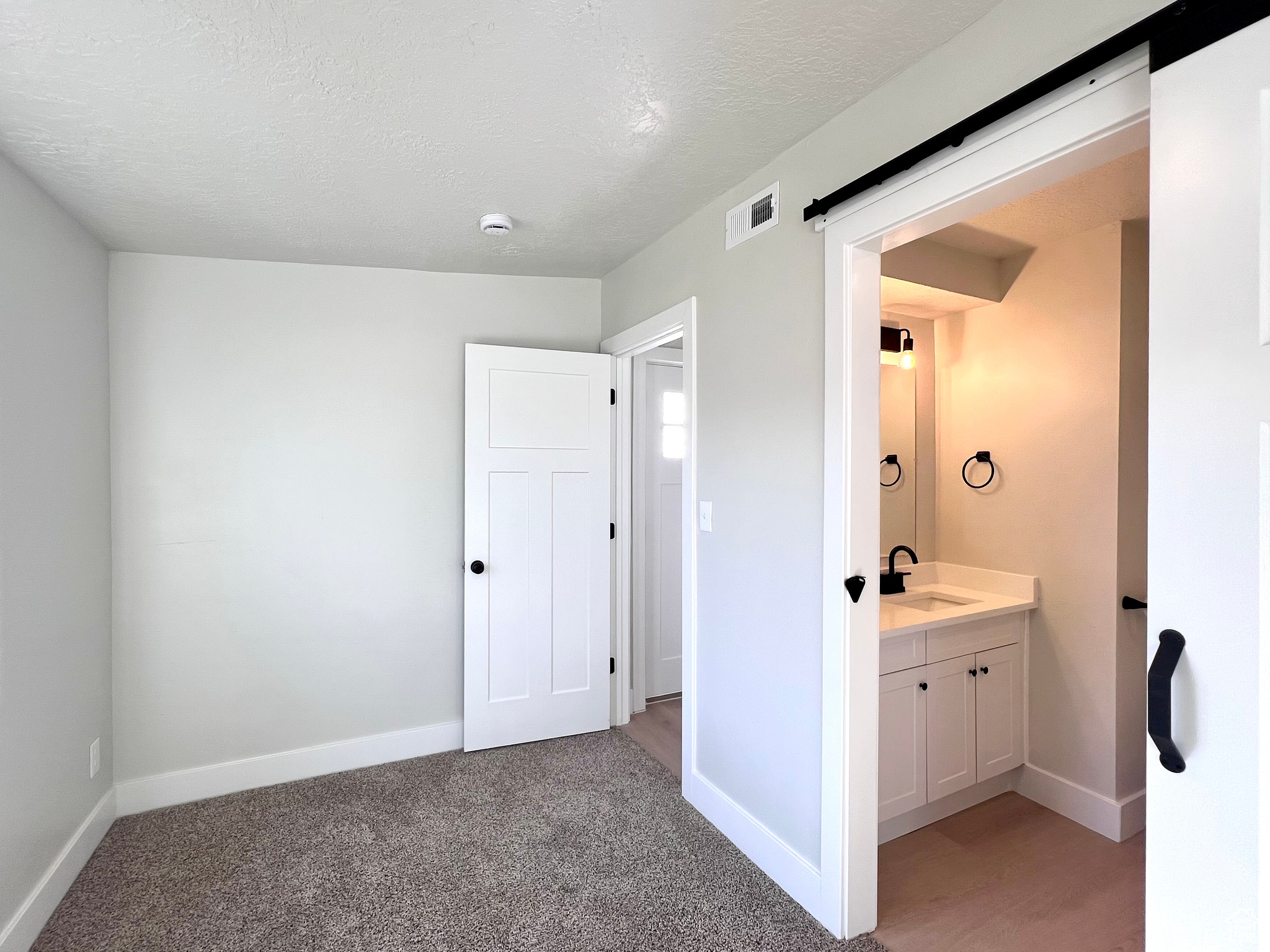 Interior space with light carpet, a textured ceiling, ensuite bathroom, and sink