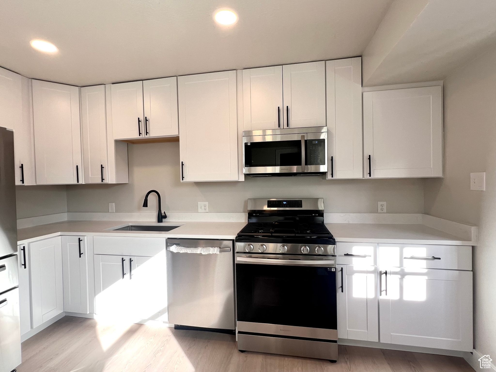 Kitchen with white cabinetry, sink, stainless steel appliances, and light wood-type flooring