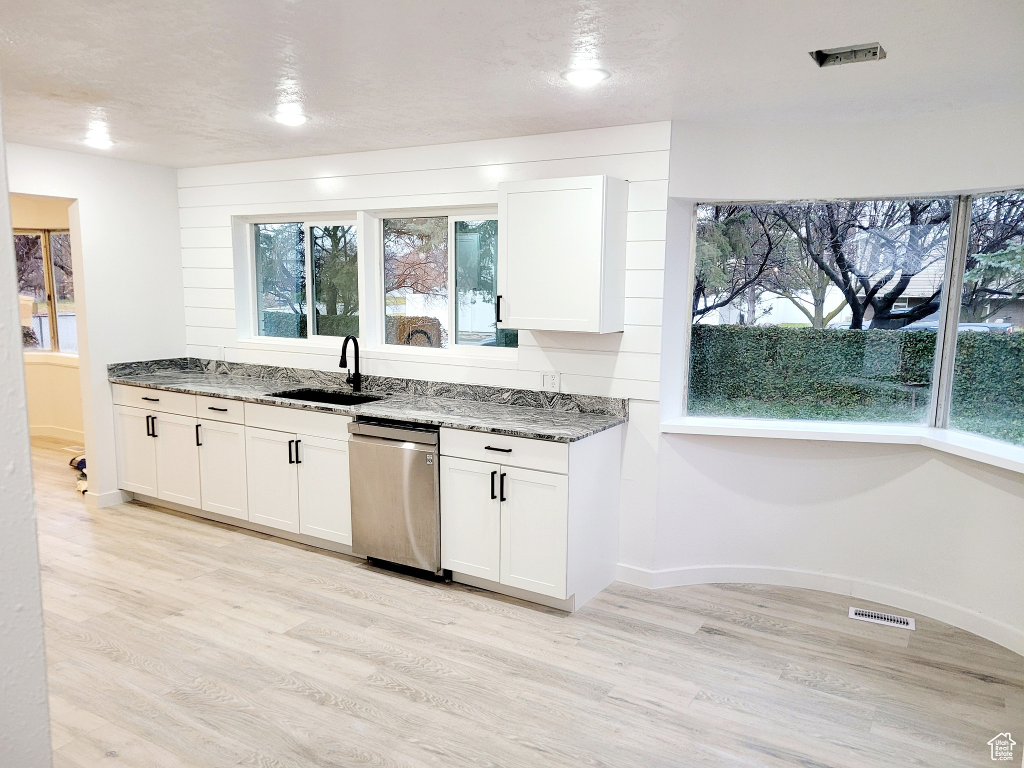 Kitchen with light stone counters, dishwasher, and white cabinets