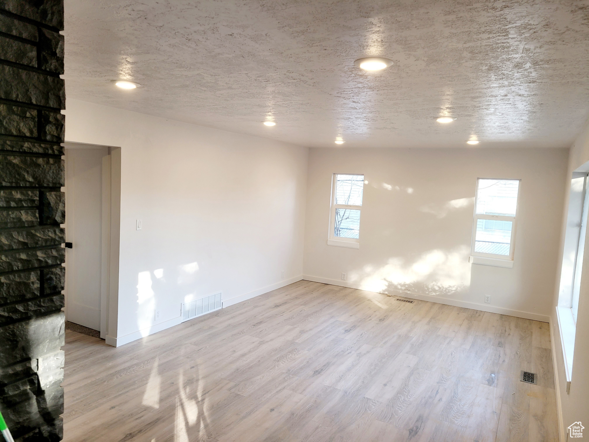 Unfurnished room with a textured ceiling, light wood-type flooring, and a healthy amount of sunlight