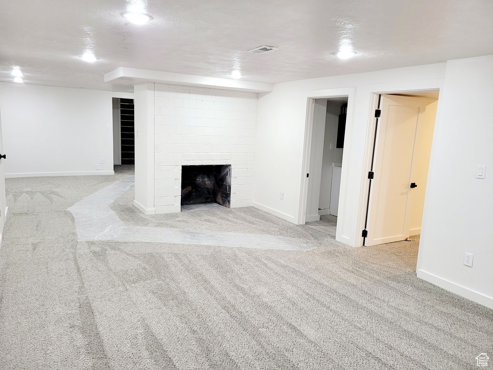 Basement featuring light colored carpet, a textured ceiling, and a brick fireplace