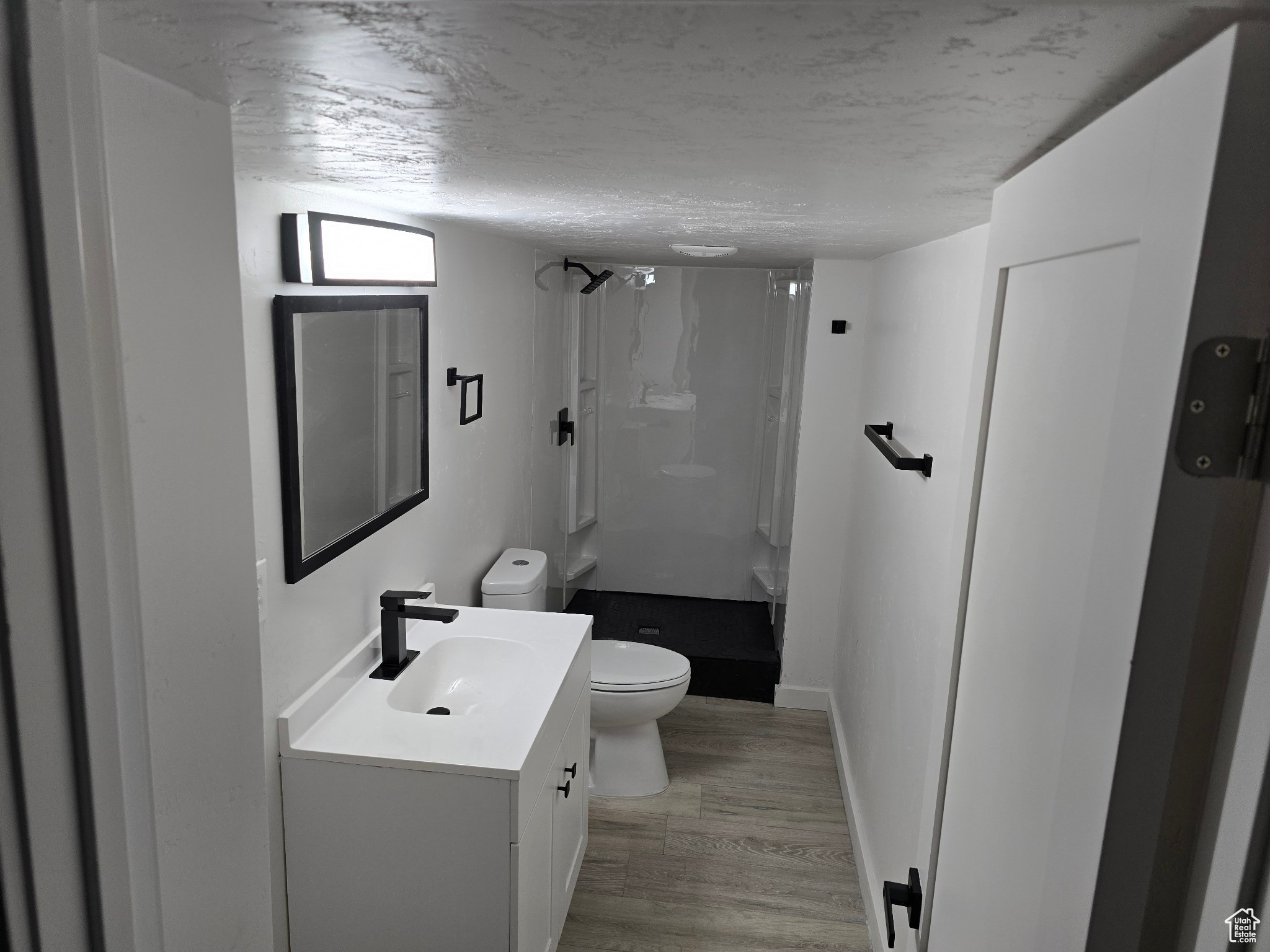 Bathroom featuring toilet, a shower, wood-type flooring, a textured ceiling, and vanity