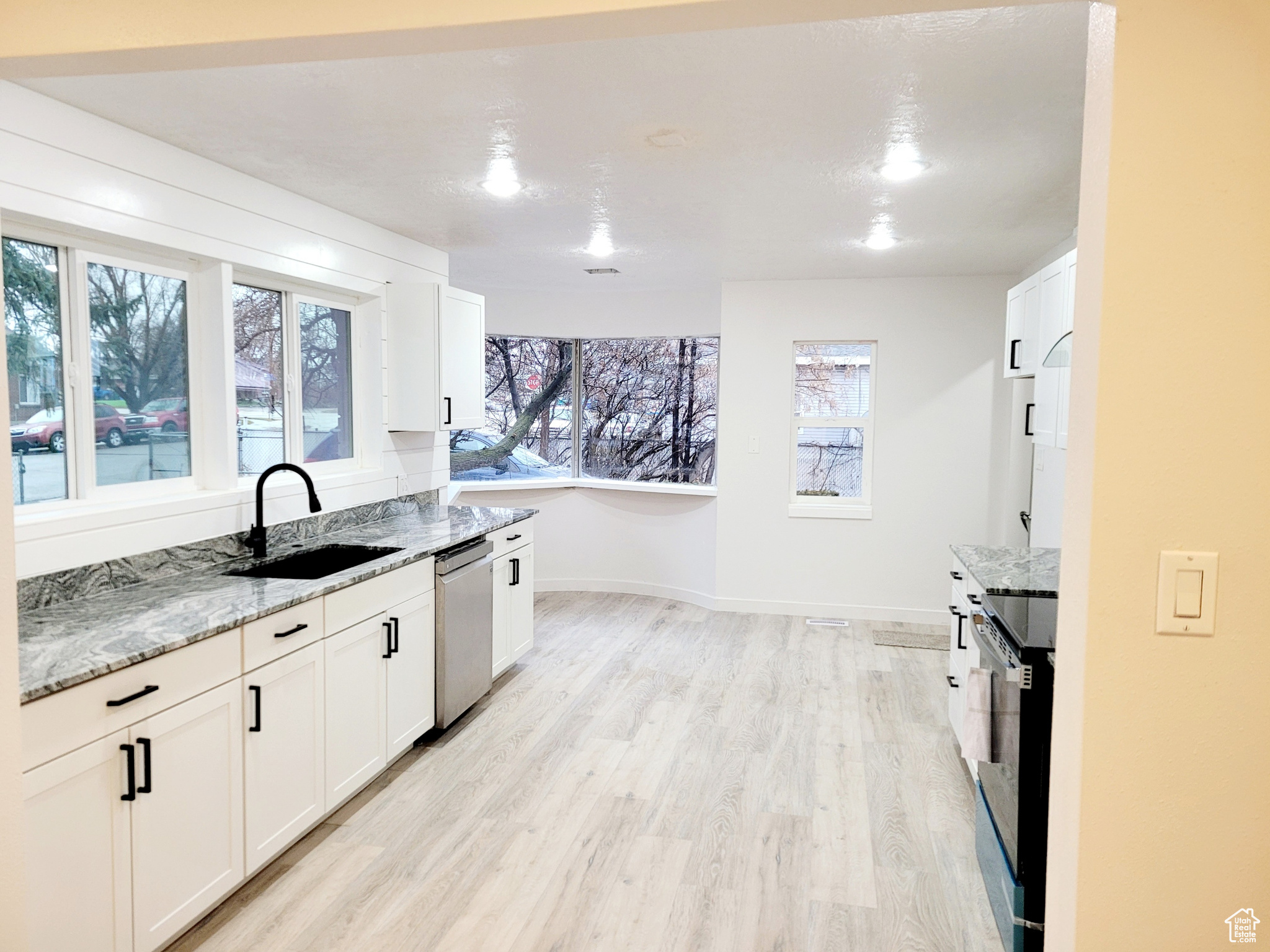 Kitchen with white cabinetry, dishwasher, sink, and light stone countertops