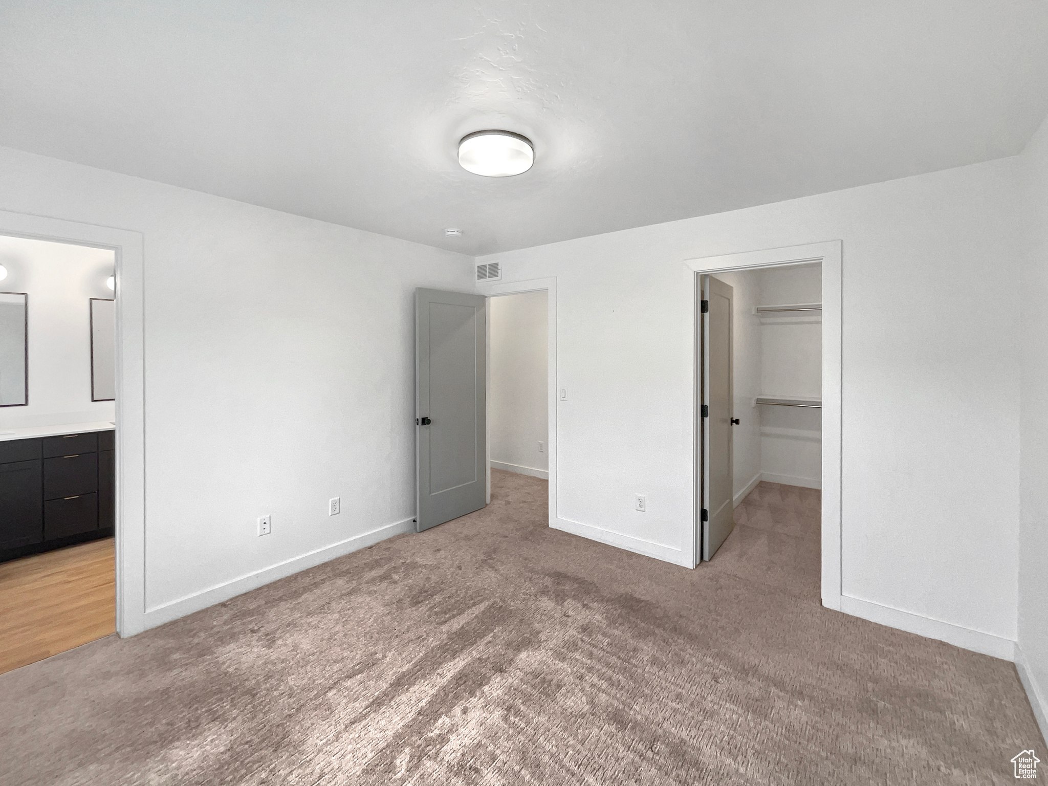 Unfurnished bedroom with a closet, a spacious closet, light carpet, and ensuite bath