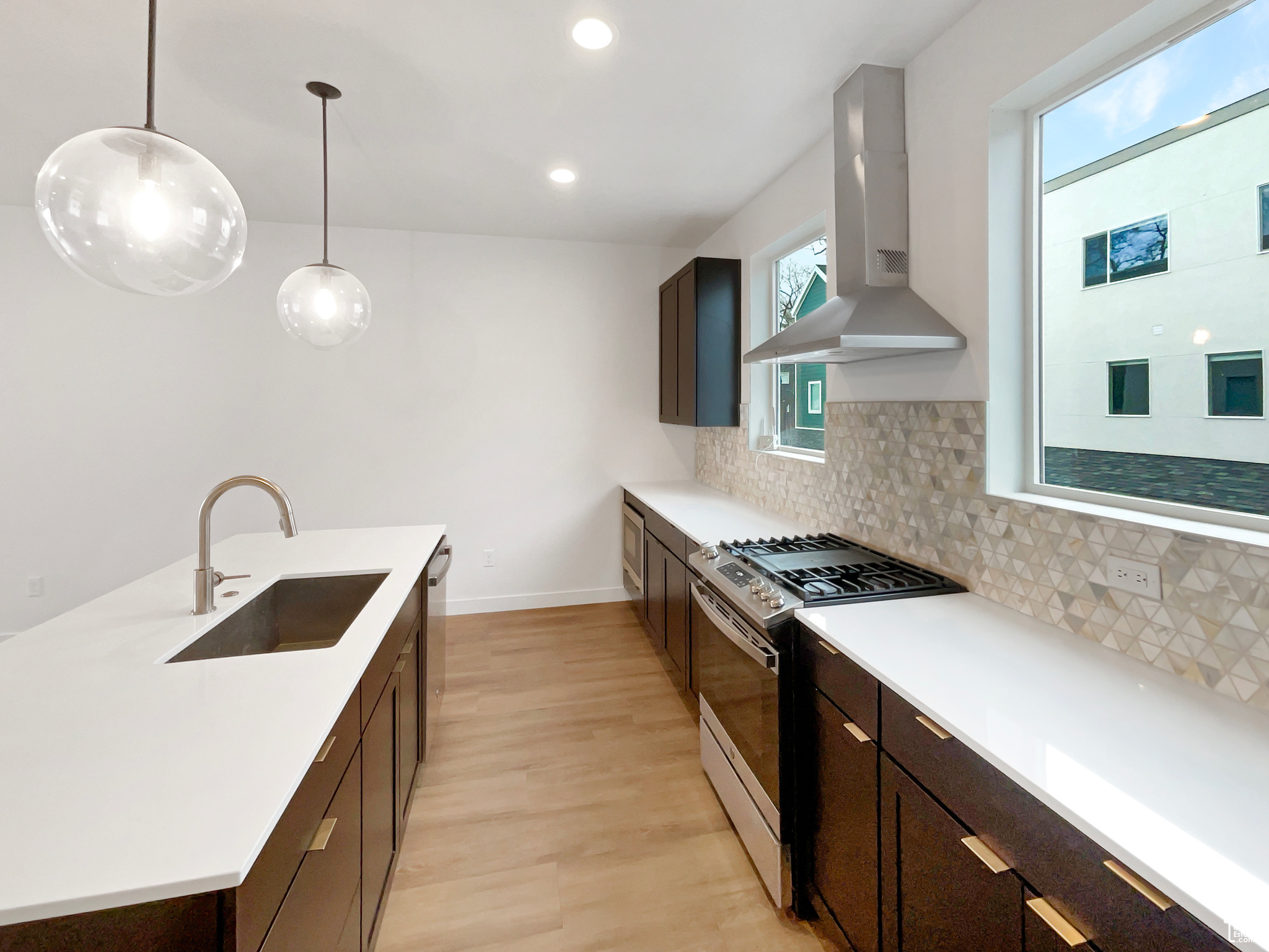 Kitchen with decorative backsplash, stainless steel appliances, sink, exhaust hood, and pendant lighting