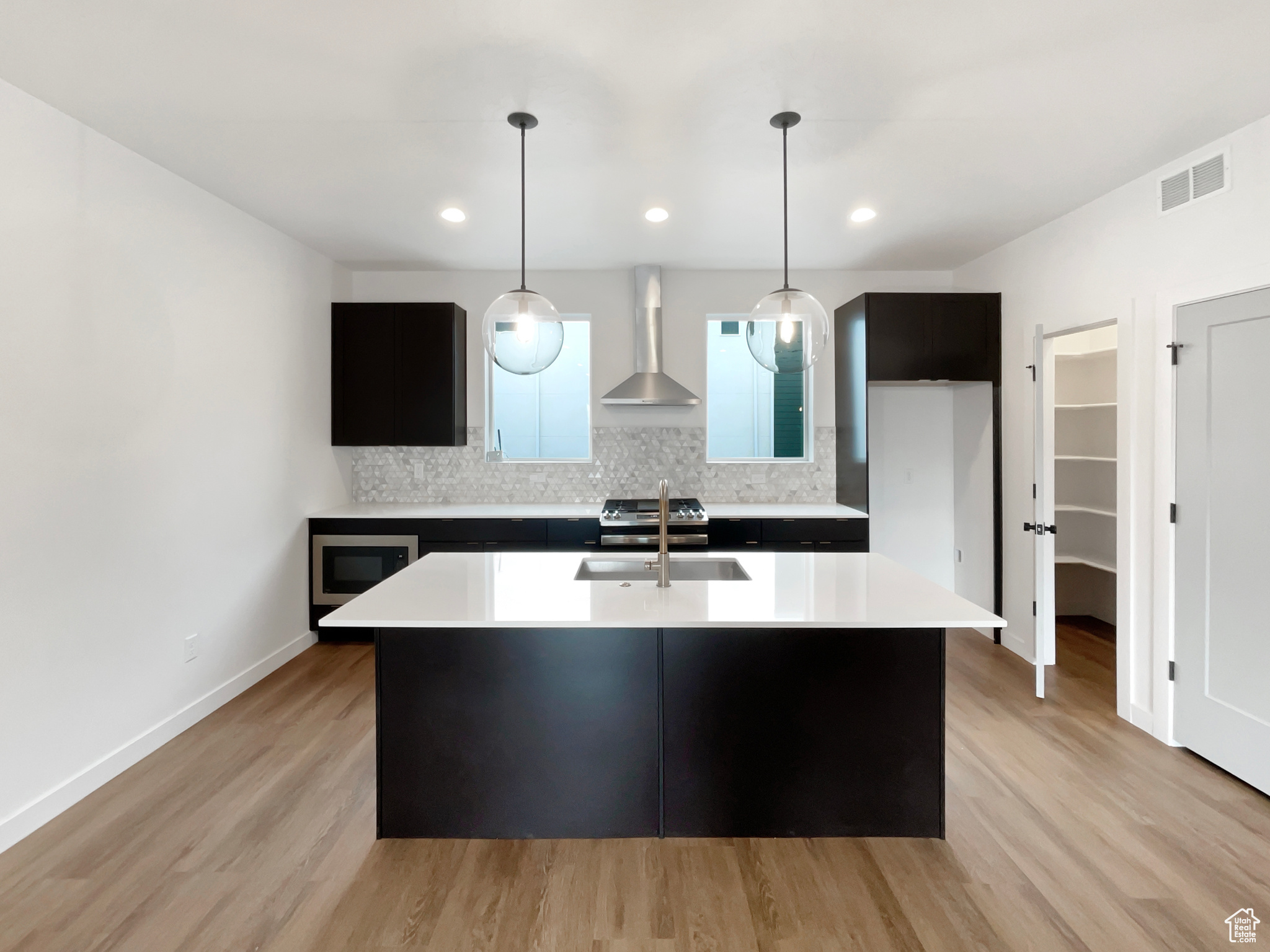 Kitchen with wall chimney exhaust hood, tasteful backsplash, an island with sink, pendant lighting, and appliances with stainless steel finishes