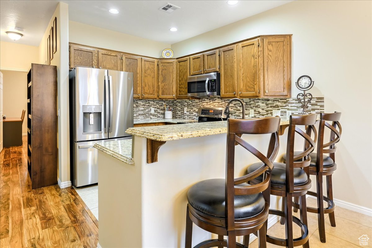 Kitchen featuring a kitchen breakfast bar, light stone counters, kitchen peninsula, and appliances with stainless steel finishes