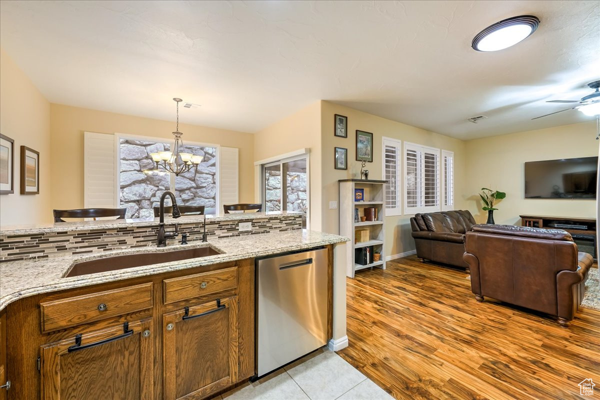 Kitchen featuring pendant lighting, dishwasher, backsplash, sink, and light stone countertops