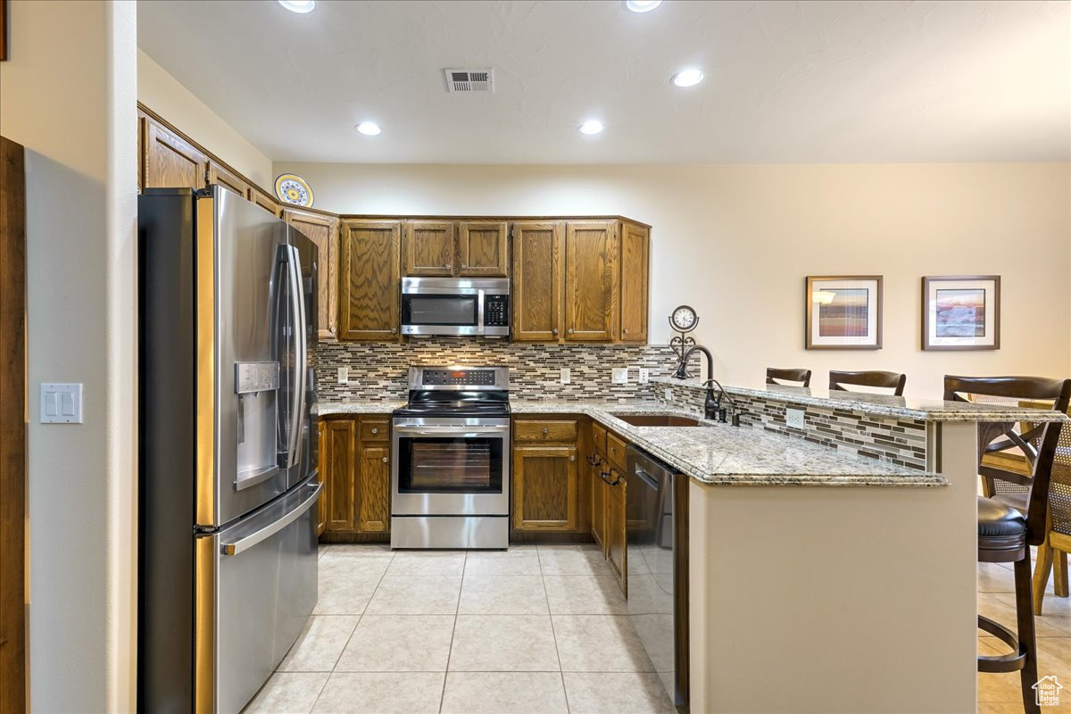 Kitchen with kitchen peninsula, light stone countertops, a breakfast bar, stainless steel appliances, and light tile patterned floors